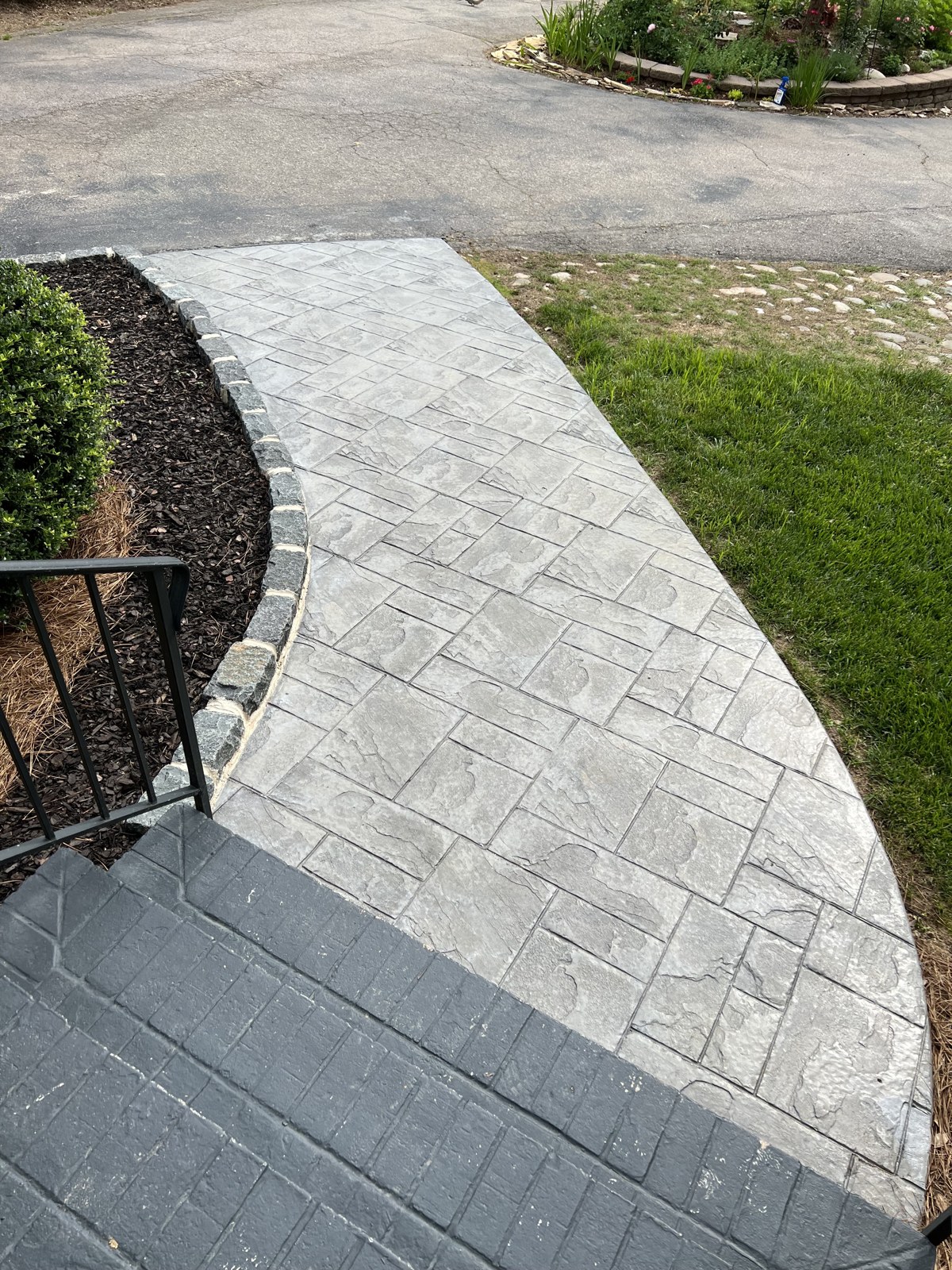 Curved textured masonry walkway beside a lawn and driveway