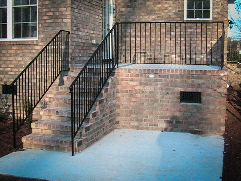 Black metal stair and landing railings at a brick entrance